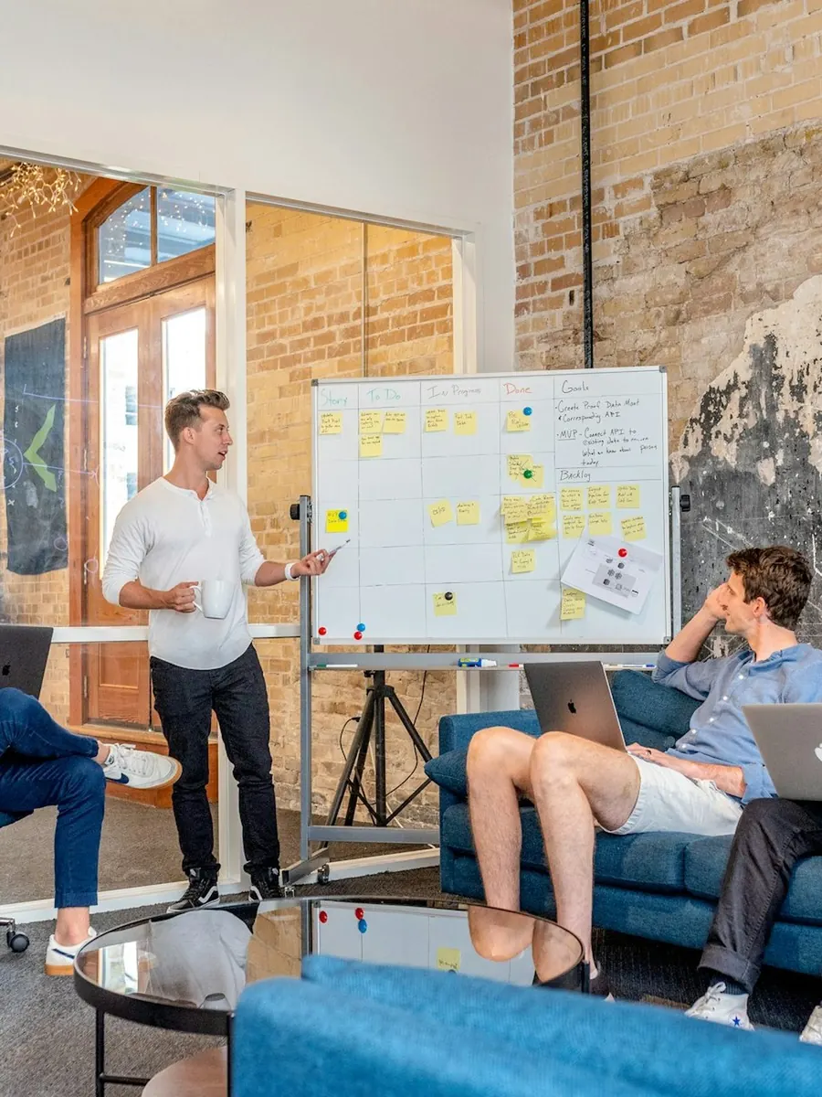 An entrepreneur leading a workshop at a whiteboard, the team on a sofa